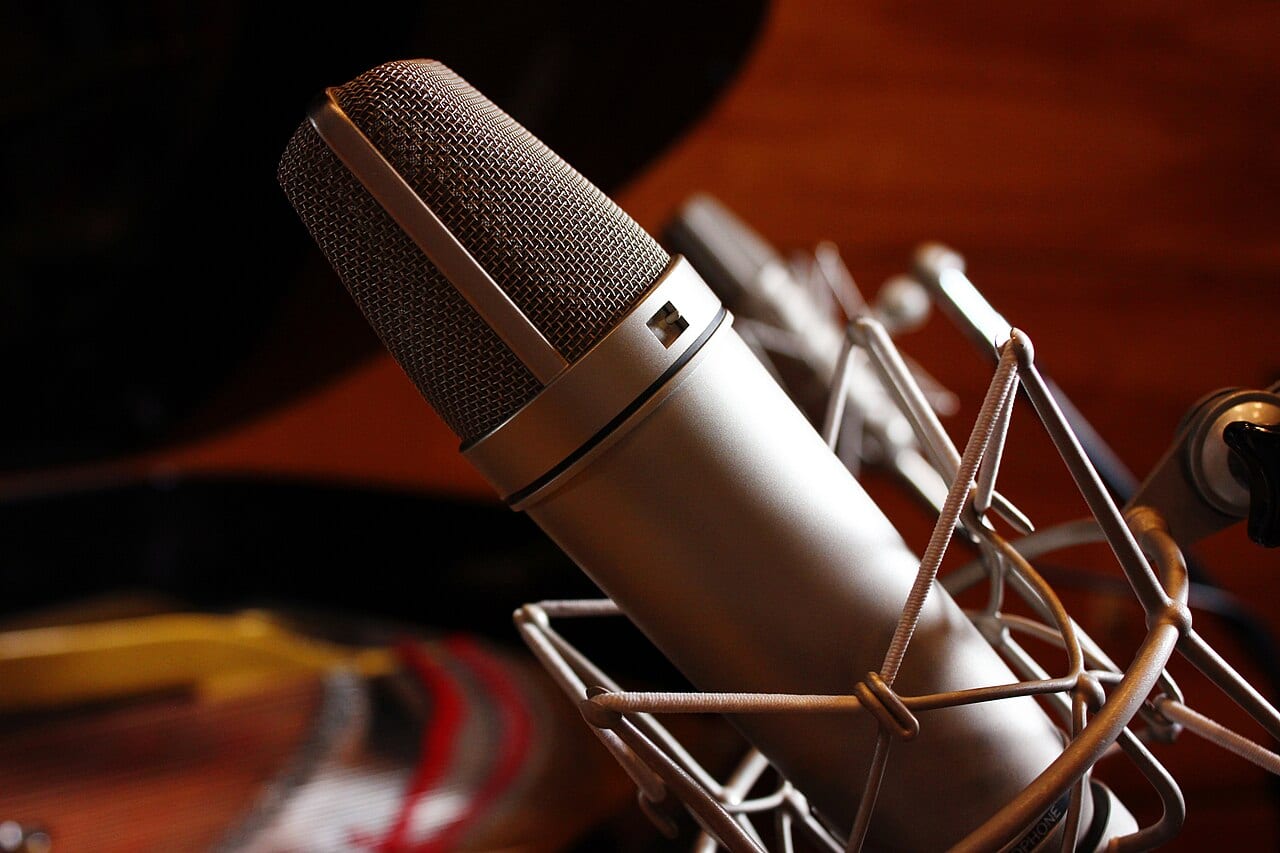 A silver studio microphone with headphones in a recording booth