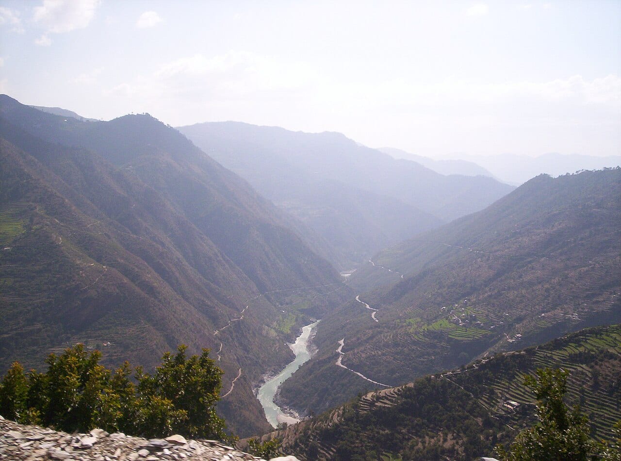 A wide river flowing below steep Himalayan mountains