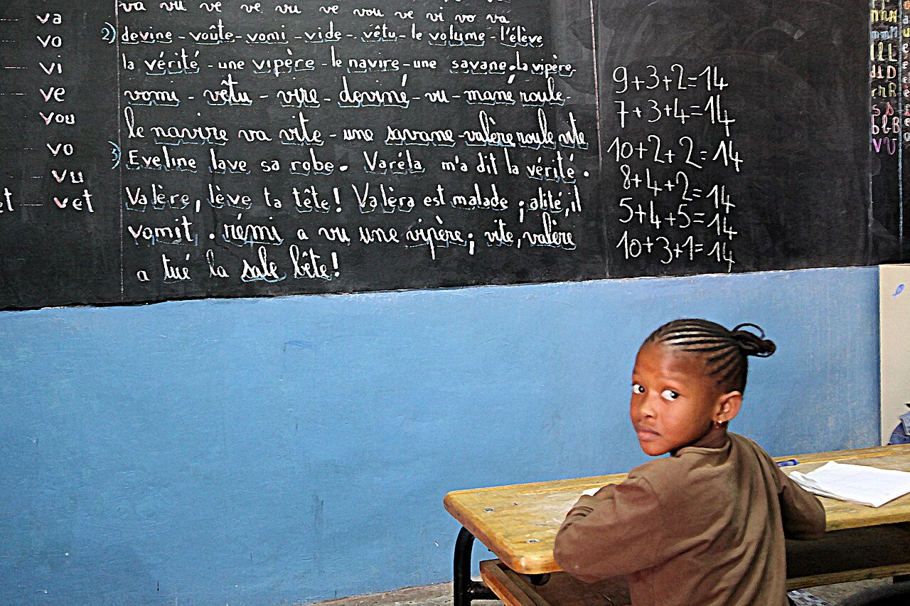 A schoolgirl at her desk in a classroom on Gorée Island, with a blackboard full of French lessons